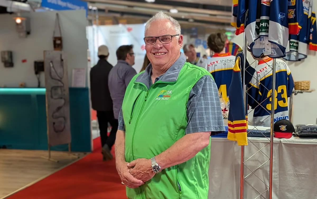 Ein Mann schaut in die Kamera, im Hintergrund die Szenerie einer Gewerbemesse.